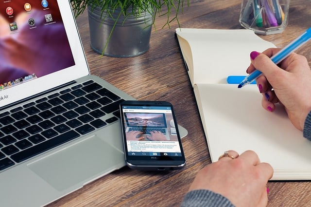 Person writing on notebook next to laptop